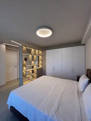 A bedroom with a large bed, built-in shelving, and a ceiling light fixture. - Crystal Green Signature Properties  (Athina)