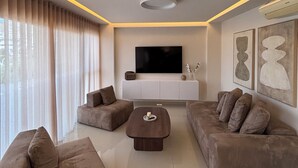 Een moderne woonkamer met een flatscreen televisie, twee banken, een salontafel en een groot raam met gordijnen.