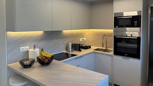 Een moderne keuken met een ingebouwde magnetron, oven en spoelbak. Op het aanrecht staat een fruitschaal en een waterkoker.