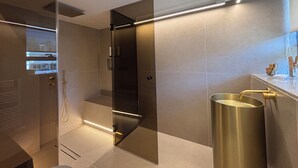 Een moderne badkamer met een glazen douchecabine, een wastafel met gouden kraan en een grote spiegel.