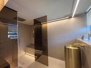 A modern bathroom with a glass shower enclosure, a vanity with a gold faucet, and a large mirror. - Crystal Green Signature Properties  (Athina)