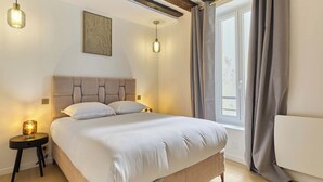 Ein Schlafzimmer mit einem Bett, Nachttischlampen, einem Fenster mit Vorhängen und einem Holzbalken an der Decke.