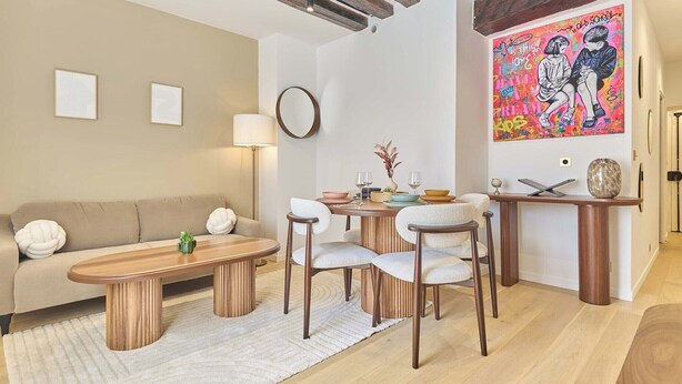 Ein modernes Wohnzimmer mit Sofa, Couchtisch und Sesseln, einem Esstisch mit Vase und einem farbenfrohen Gemälde an der Wand.