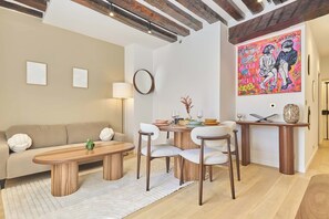 A modern living room with a sofa, coffee table, and chairs, a dining table with a vase, and a colorful painting on the wall. - Charming apartment in Le Marais Center of Paris (Paris)