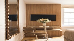 Ein modernes Schlafzimmer mit einem großen Spiegel, einer Couch, einem kleinen Tisch mit Blumen und einem an der Wand befestigten Fernseher.