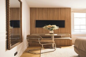 A modern bedroom with a large mirror, a sofa, a small table with a vase of flowers, and a television mounted on the wall. - Sublime Suite Saint Honoré, Elysée Palace (Paris)