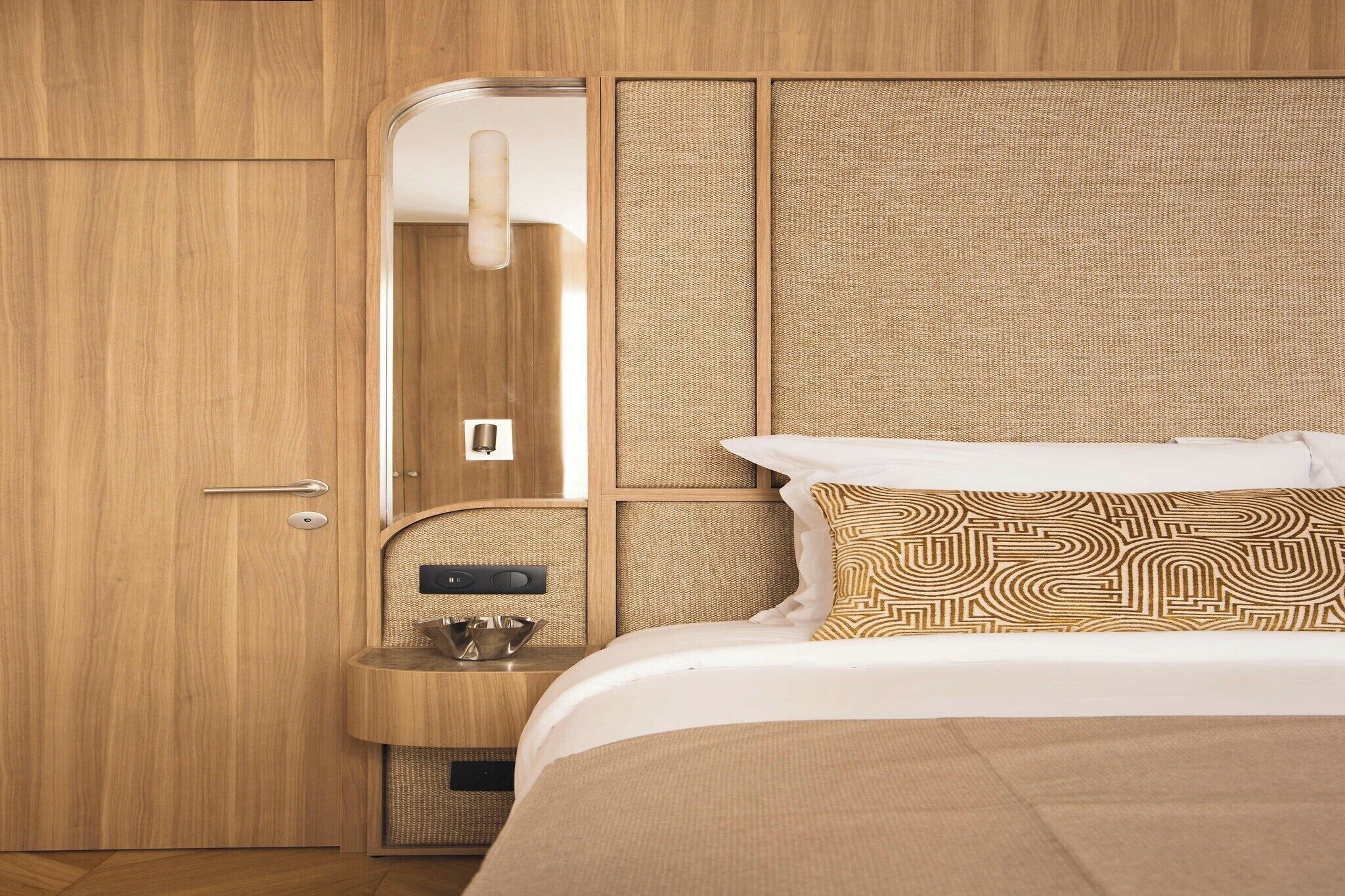 A hotel room with a wooden wardrobe, a built-in vanity with a mirror, and a bed with patterned pillows.