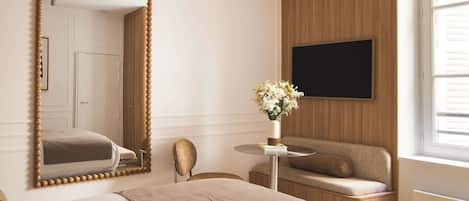Una camera d'albergo con un grande specchio, un divano, un tavolino con un vaso di fiori e una televisione montata a parete.