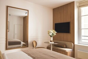 A hotel room with a large mirror, a sofa, a small table with a vase of flowers, and a television mounted on the wall. - Sublime Suite Saint Honoré, Elysée Palace (Paris)