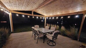 An outdoor patio with a wooden ceiling, string lights, a table and chairs, and a view of the night sky. - Serene 2-bedroom house with AC in charming Houghton Lake (Houghton Lake)