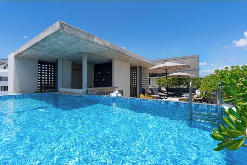 Une piscine dotée de chaises longues et de parasols, un espace de détente couvert et un bâtiment au style architectural moderne.