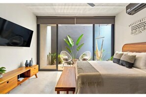 Une chambre moderne avec un lit, une télévision, un banc en bois et une grande fenêtre.