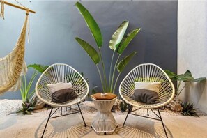 Two wicker chairs with cushions, a small wooden table, and large green plants in a sunlit outdoor area. - Ocean Boutique Condos (Playa del Carmen)