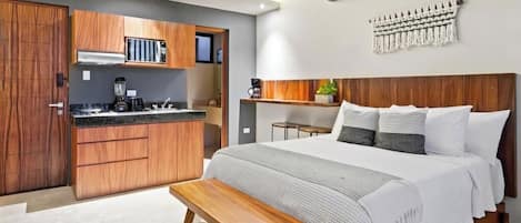 A modern bedroom with a wooden bed, a bench, a small kitchenette, and a wall-mounted air conditioner.