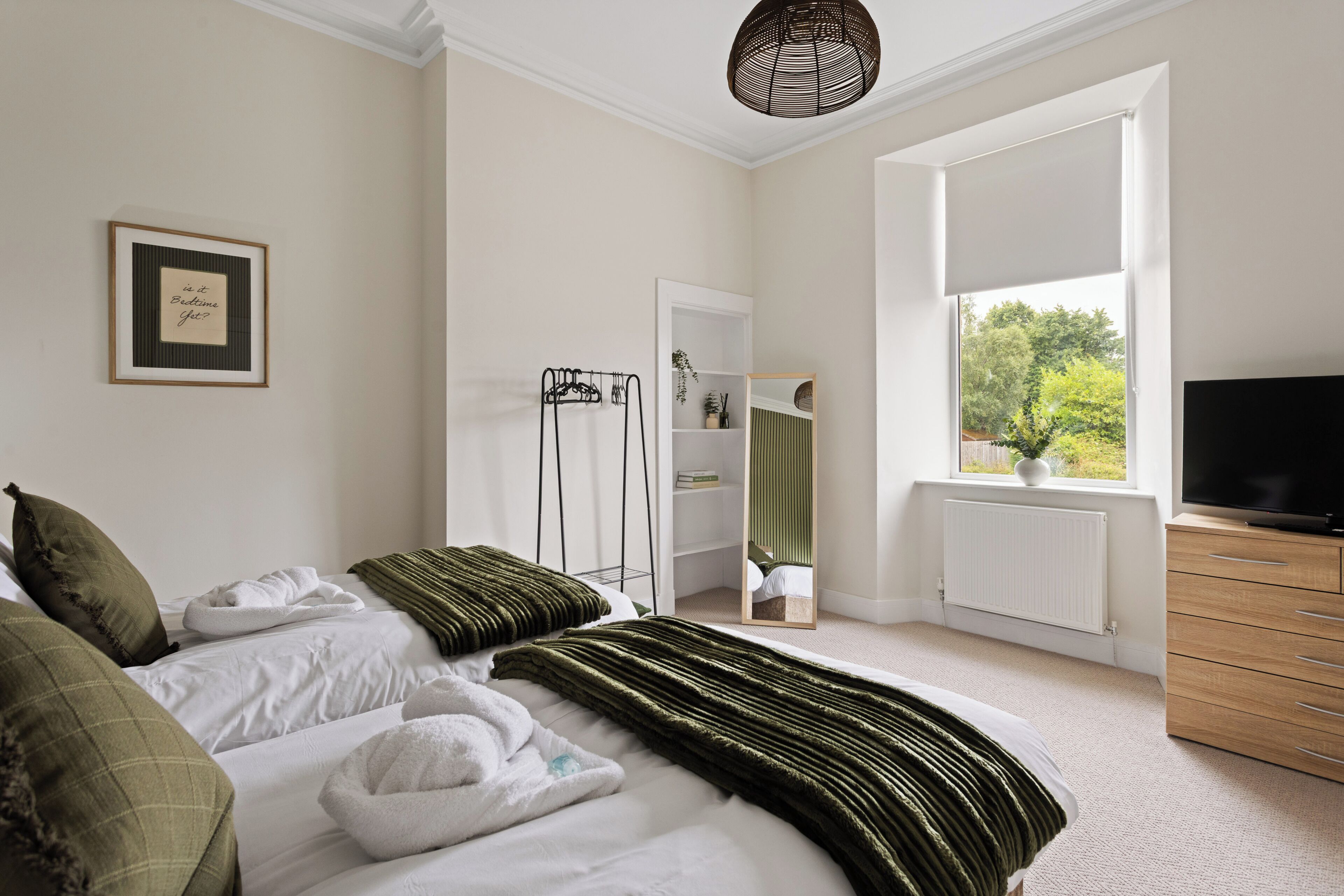 A bedroom with a bed, a TV, a window, and a mirror.