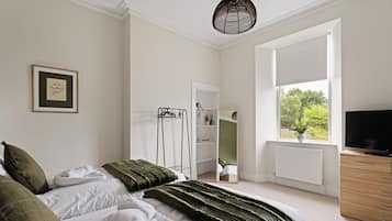 A bedroom with a bed, a TV, a window, and a mirror.