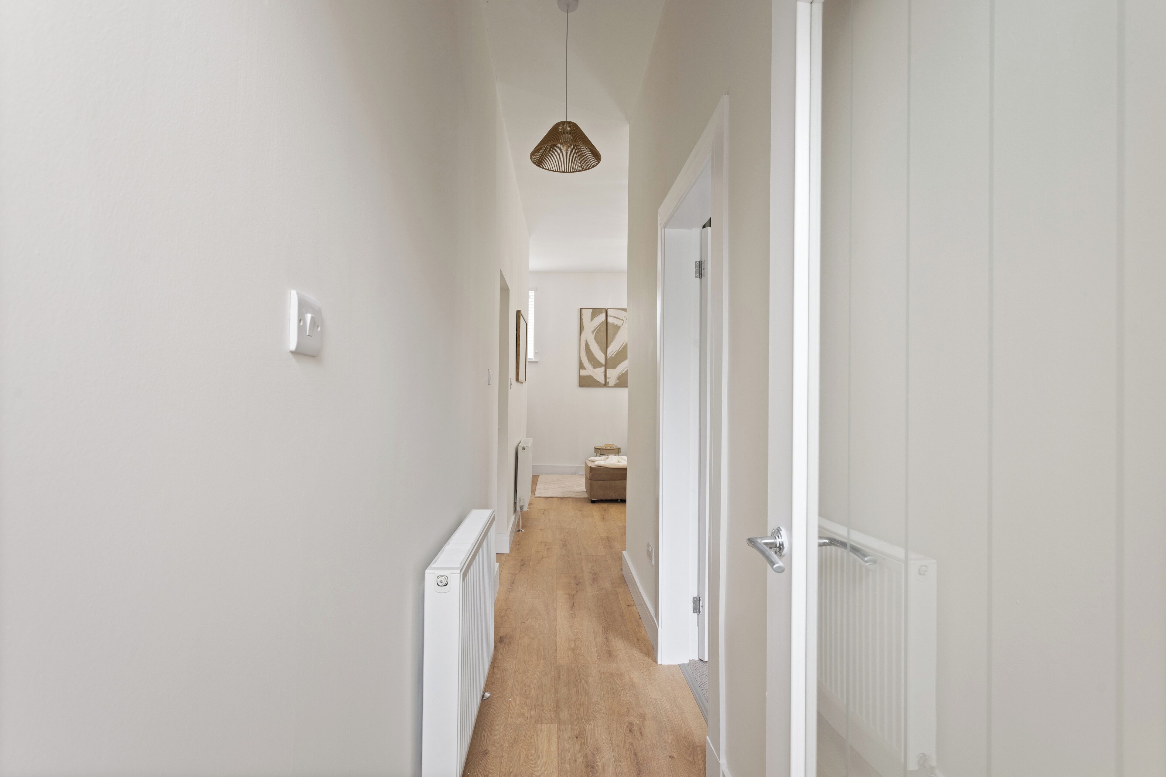 Un couloir aux murs blancs, doté d’un plancher en bois, d’un luminaire suspendu et d’un radiateur.