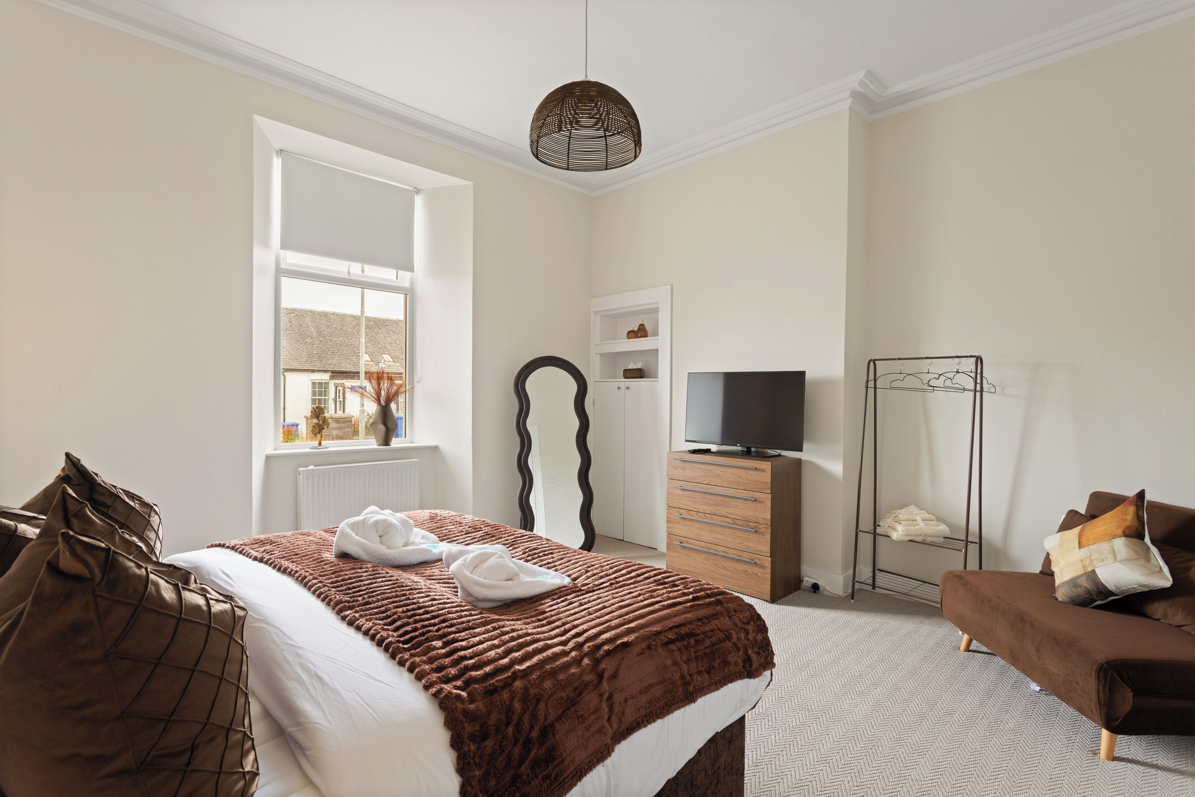 Quarto de hotel com cama, televisão, penteadeira, espelho e janela.