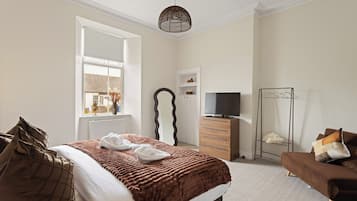 Quarto de hotel com cama, televisão, penteadeira, espelho e janela.