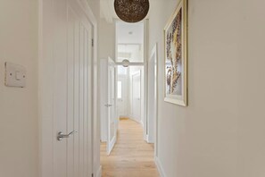 A hallway with white doors, a hanging light fixture, and a framed artwork on the wall.