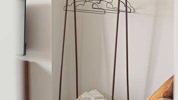 A room with a metal wire shelf unit against a wall, a television mounted on the wall, and a bed with a brown cover.