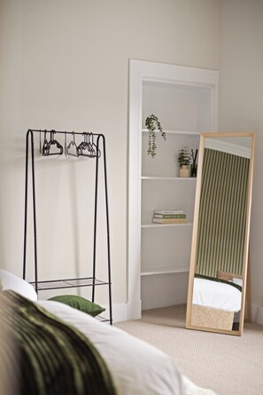 A bedroom with a bed, a metal drying rack, a mirror, and a bookshelf.