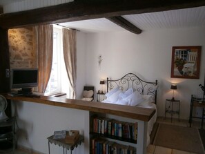 A bedroom with a bed, bedside table, lamp, and a bookshelf. - A romantic getaway on the square in Saint-Chinian, featuring fantastic hiking and wine (saint-chinian)