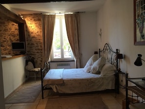 A bedroom with a bed, a chair, a desk, and a window with curtains. - A romantic getaway on the square in Saint-Chinian, featuring fantastic hiking and wine (saint-chinian)