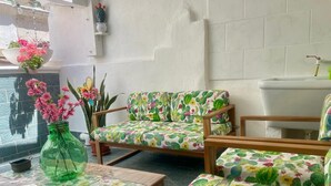Una habitación con sofá estampado de cactus, un jarrón verde con flores rosas y una pared de azulejos.