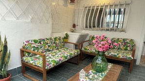 Una habitación con dos sofás de madera tapizados con motivos de cactus, una mesa de centro de madera y un jarrón con flores rosas.