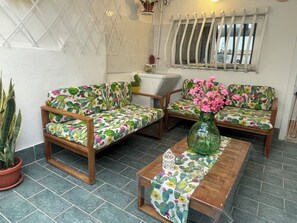A room with two wooden sofas with cactus-patterned upholstery, a wooden coffee table, and a vase with pink flowers. - A small house 5 minutes from the beach, with a beautiful terrace, in the city center (Monopoli)