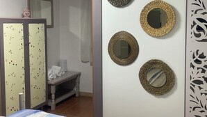 Una habitación con cama, un armario de motivos florales, un banco y una pared con espejos decorativos.