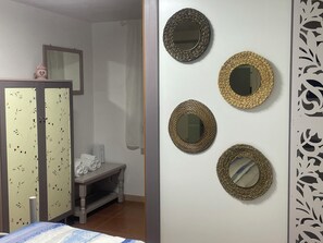 A room with a bed, a wardrobe with floral patterns, a bench, and a wall with decorative mirrors. - A small house 5 minutes from the beach, with a beautiful terrace, in the city center (Monopoli)