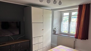 Ein Schlafzimmer mit einem Bett, einem Kleiderschrank, einem Fernseher und einem Fenster mit Vorhängen.