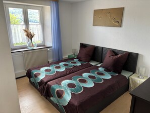 A bedroom with a bed, a window with curtains, a radiator, a bedside table, and a wall-mounted artwork. - "Am Bückle" Vacation Rental with a View of the Rhine – Accommodates up to 4 People and Pets (Laufenburg (Baden))