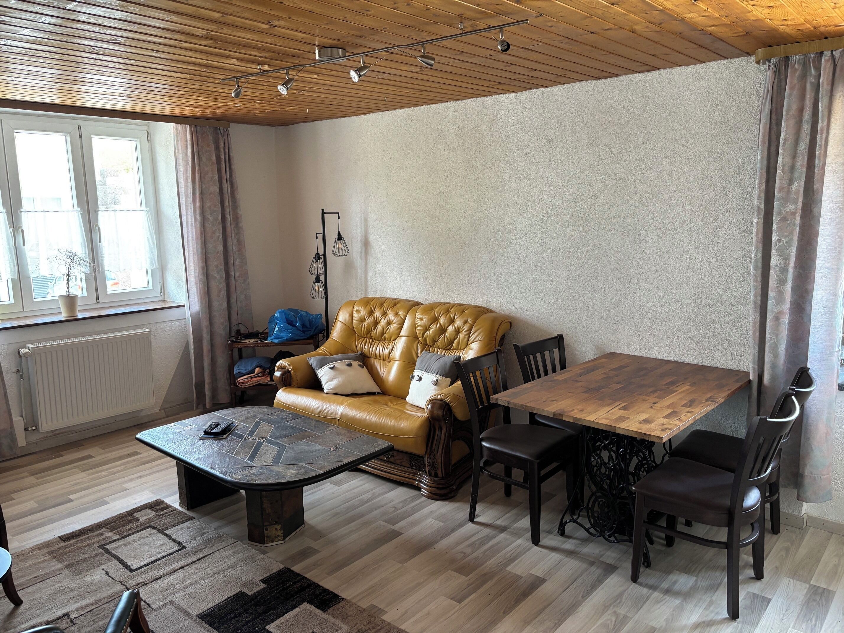 Ein Wohnzimmer mit einem Ledersofa, einem Holztisch und einem Esstisch mit Stühlen.