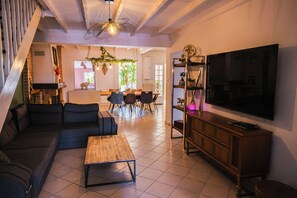 Ein modernes Wohnzimmer mit Sofa, Couchtisch, Fernseher und einem Essbereich mit Stühlen und Tisch.