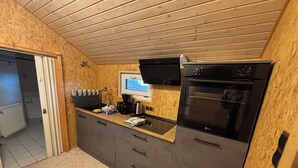 Een compacte keuken met een ingebouwde oven, een koffiezetapparaat en een raam boven de gootsteen.