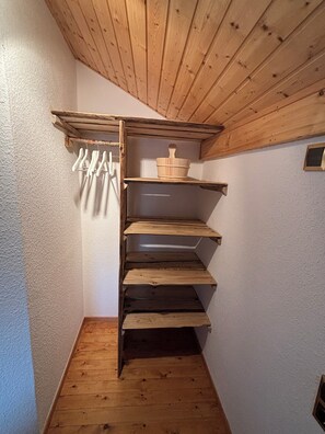 A wooden staircase leading to a lofted storage area with shelves and a hanging rack. - Tiny House with a Garden and Sauna (Karbach)