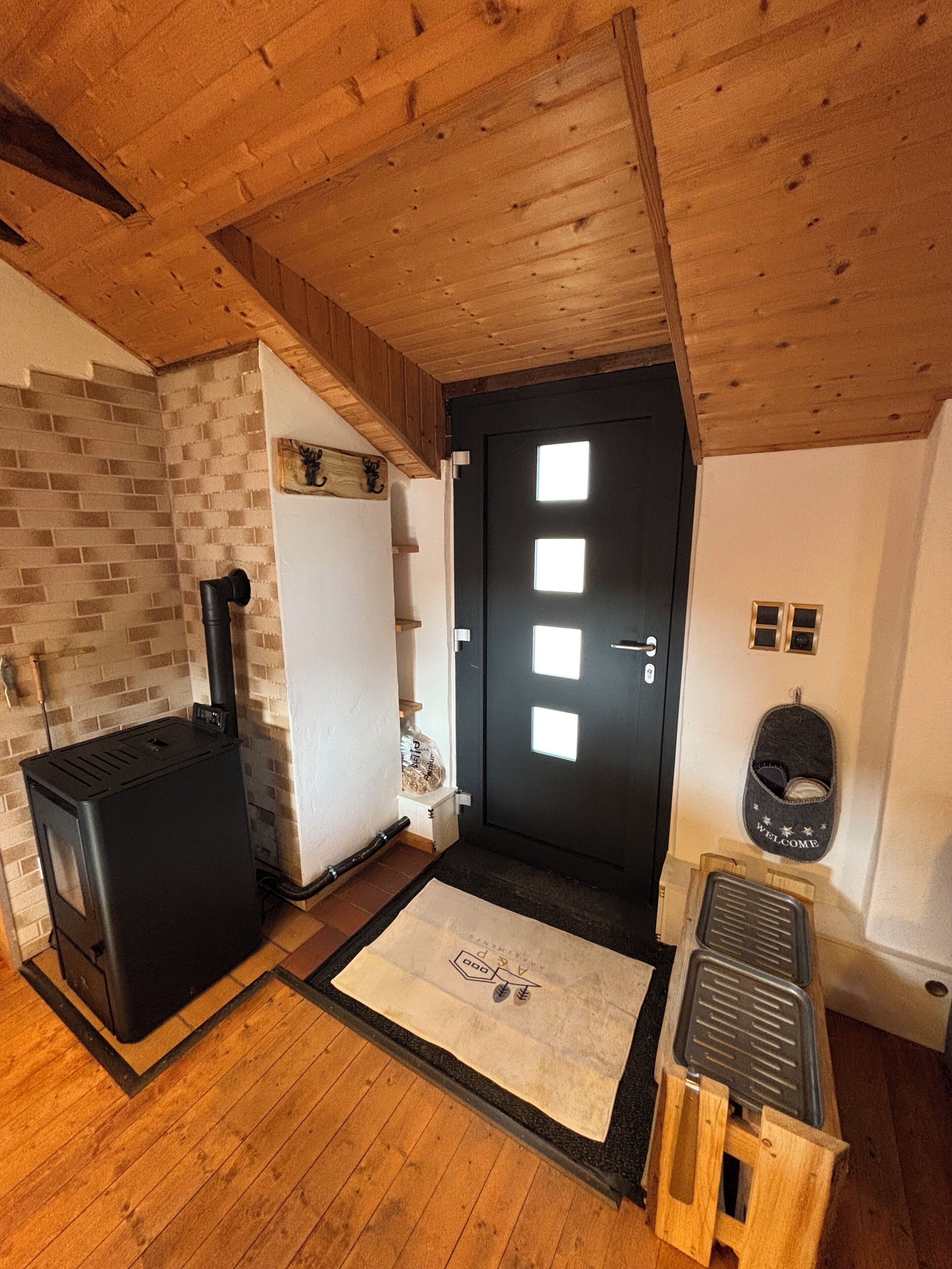 A room with a black stove, a door with square windows, and a welcome mat.