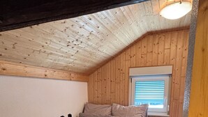 Een knus kamertje met een bed, een raam met zonwering en houten wanden.