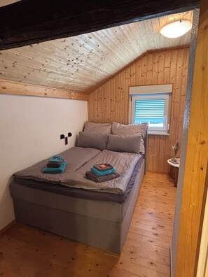 A small, cozy room with a bed, a window with blinds, and wooden walls. - Tiny House with a Garden and Sauna (Karbach)