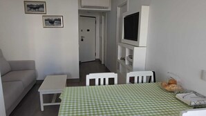 A compact living space with a sofa, a small table, a dining table with chairs, and a flat-screen TV mounted on the wall. - Rocha's Corner (Portimão)