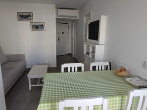 A compact living space with a sofa, a small table, a dining table with chairs, and a flat-screen TV mounted on the wall. - Rocha's Corner (Portimão)