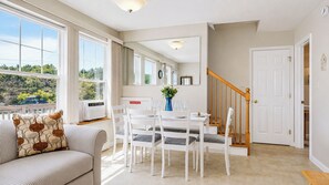 A spacious living area with a dining table, white chairs, a sofa with patterned cushions, and a staircase leading to another level.