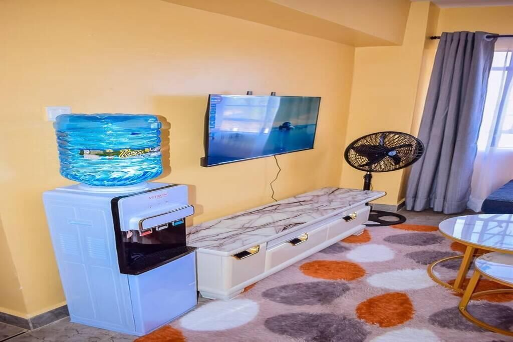 Une pièce équipée d’un distributeur d’eau, d’une télévision, d’un ventilateur, d’un banc en marbre et d’un tapis à motifs.