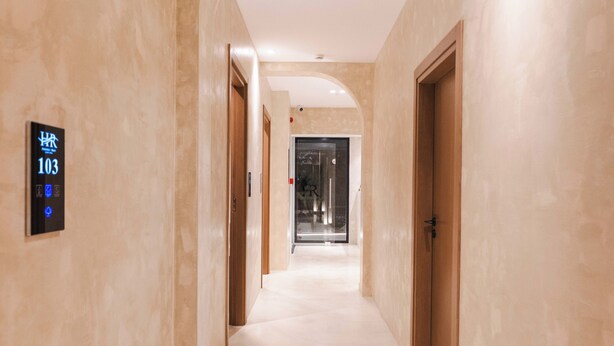 A corridor with a digital display indicating room number 103, a glass door at the end, and a wooden door on the right.