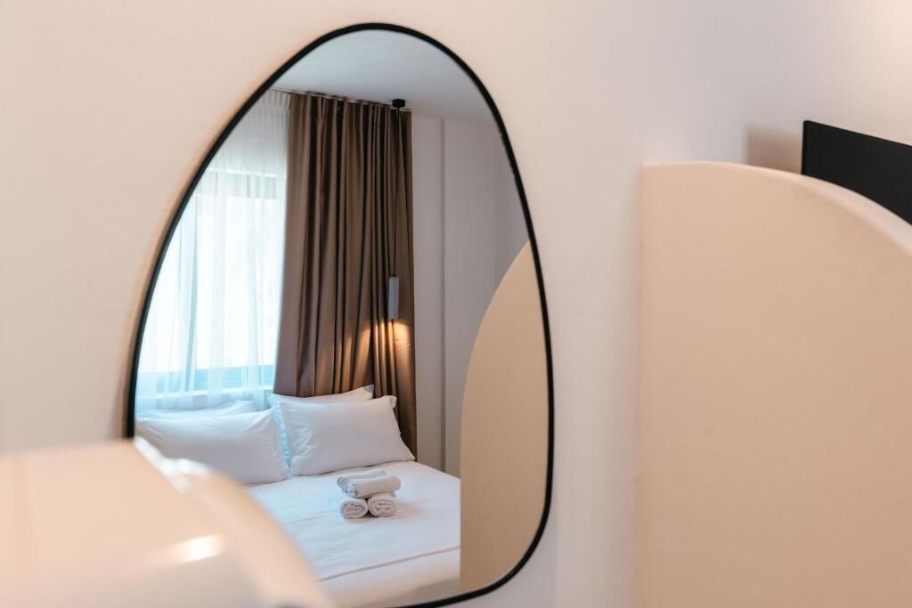 A hotel room with a bed, a mirror, and a window with curtains.