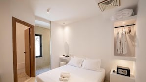 A modern bedroom with a large bed, a bedside table with a radio, and a clothing rack with robes.