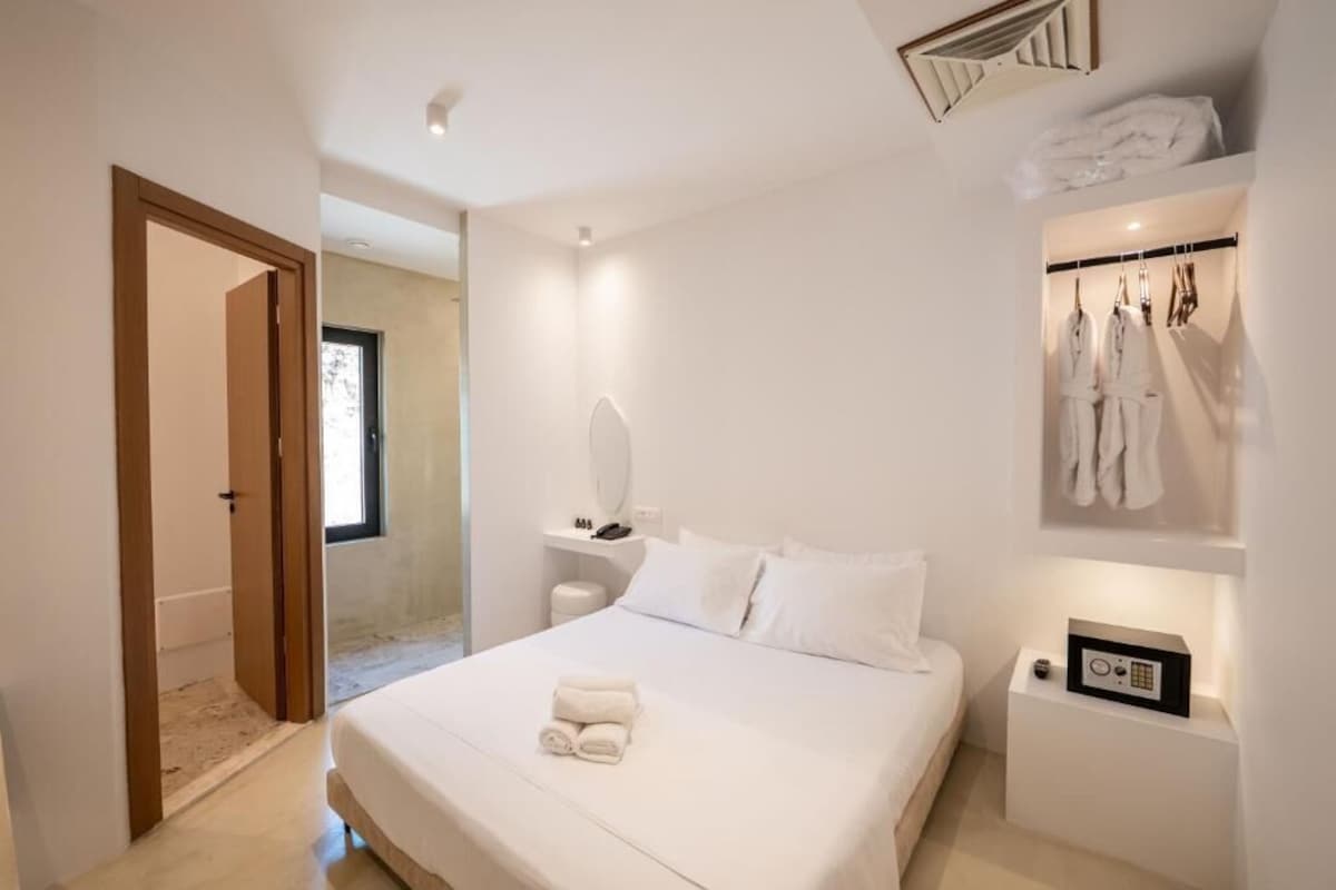 A modern bedroom with a large bed, a bedside table with a radio, and a clothing rack with robes.